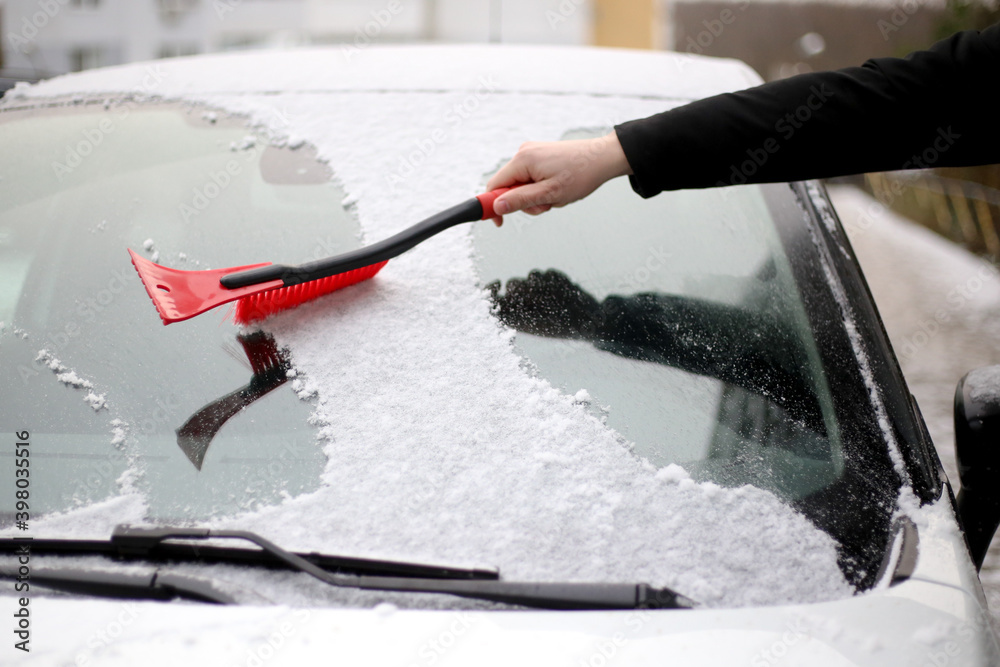 a man cleans snow from the windshield of a car with a red brush a man cleans snow from the windshield of a car with a red brush