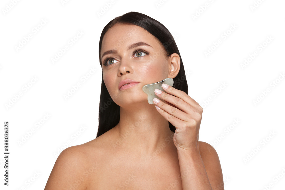 Beautiful girl with natural makeup and clean skin. Holds in hand a jade face scrubber for slimming anti aging wrinkles. Massage instrument for body skin care. Detox facial massager Beautiful girl with natural makeup and clean skin. Holds in hand a jade face scrubber for slimming anti aging wrinkles. Massage instrument for body skin care. Detox facial massager