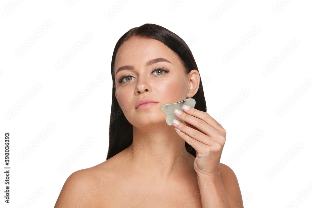 Beautiful girl with natural makeup and clean skin. Holds in hand a jade face scrubber for slimming anti aging wrinkles. Massage instrument for body skin care. Detox facial massager Beautiful girl with natural makeup and clean skin. Holds in hand a jade face scrubber for slimming anti aging wrinkles. Massage instrument for body skin care. Detox facial massager