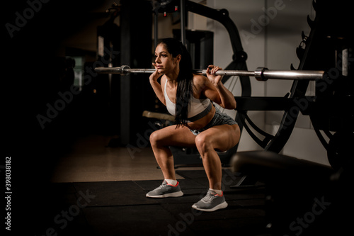 handsome strong muscular woman bodybuilder with barbell doing squats in gym.