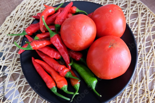 Red vegetables on a black plate. Organic tomatoes with peppers on wooden background. Summer or autumn concept. Natural food. It is called 