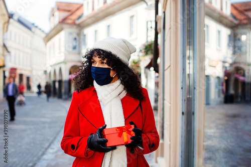 Portrait of a woman in red shopping outside with face mask holding Christmas walking by a shop store front window