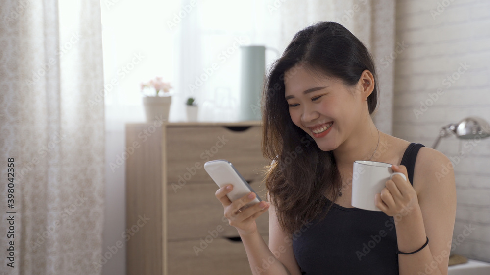 portrait of pretty asian japanese lady having morning coffee and watching funny videos on phone online while relaxing in bed. portrait of pretty asian japanese lady having morning coffee and watching funny videos on phone online while relaxing in bed.