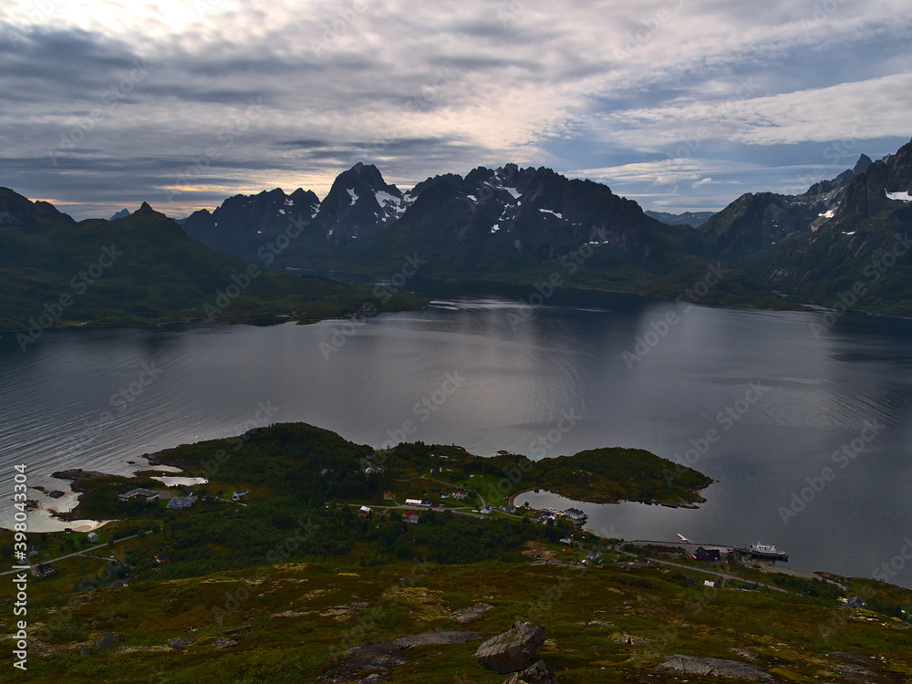 Aerial view of small fishing village Digermulen on the shore of Raftsundet strait with the majestic mountains of Austvågøya island, Lofoten, Norway viewed from peak of Keiservarden on cloudy day.