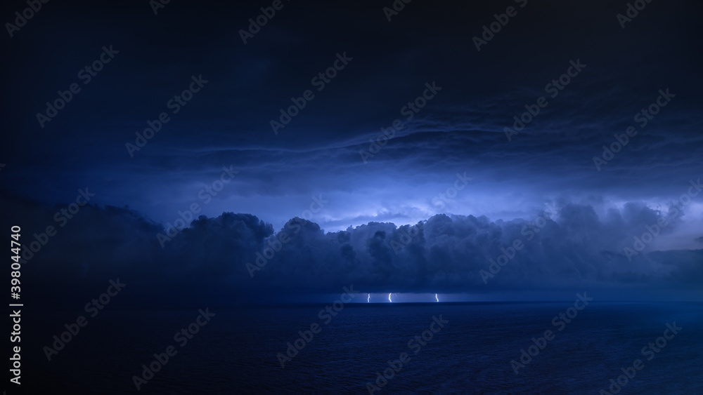 A distant thunderstorm front over the sea with three lightning bolts