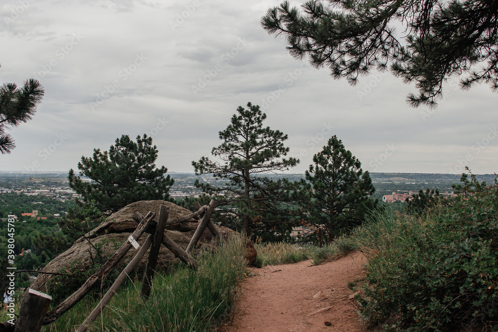 Wooden fence on the top of the mountain near a small path between the trees. Mountain landscape on a cloudy summer day