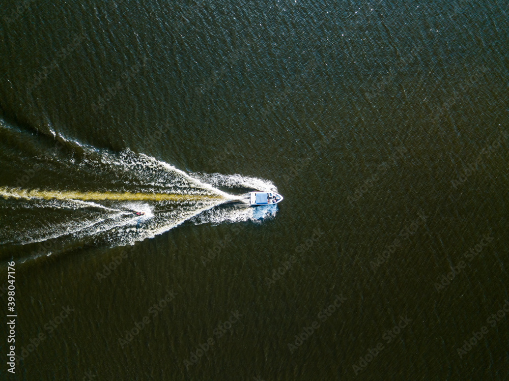 Naklejka premium Aerial drone view. Wake surfing behind a boat on the river on a sunny summer day.