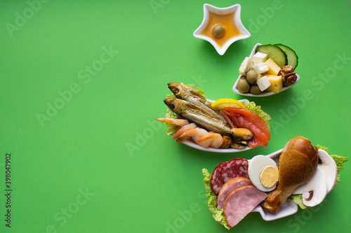 Plate in the form of a Christmas tree with protein food - meat, fish, cheeses, nuts, etc. Green background. The concept of keto diet treats for the holiday. Copy space