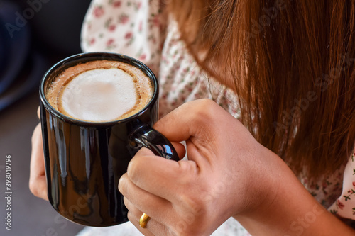 Close-up view, Warm coffee in black mug with holding hand.