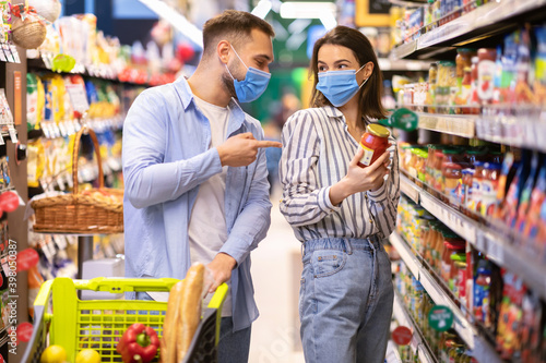 Young couple in masks shopping in supermarket