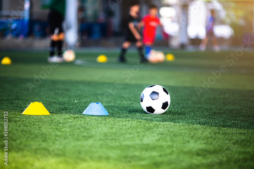 Selective focus to football with blurry marker cones on green artificial turf. Soccer equipment in soccer academy.