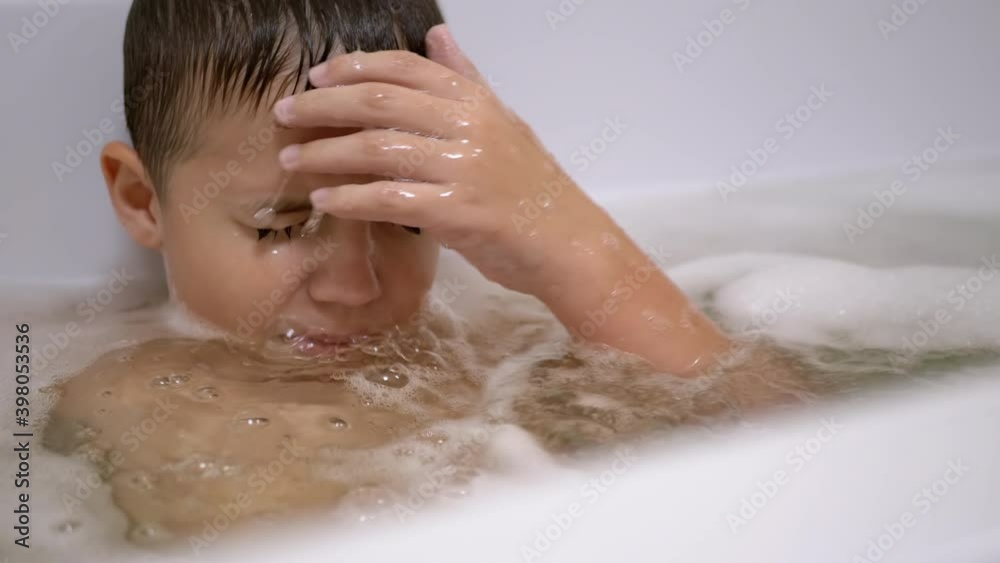 Boy Bathes in Foam Water in Bathtub, Submerges Under Water, Blows Bubbles Close-up. Boy Bathes in Foam Water in Bathtub, Submerges Under Water, Blows Bubbles Close-up.