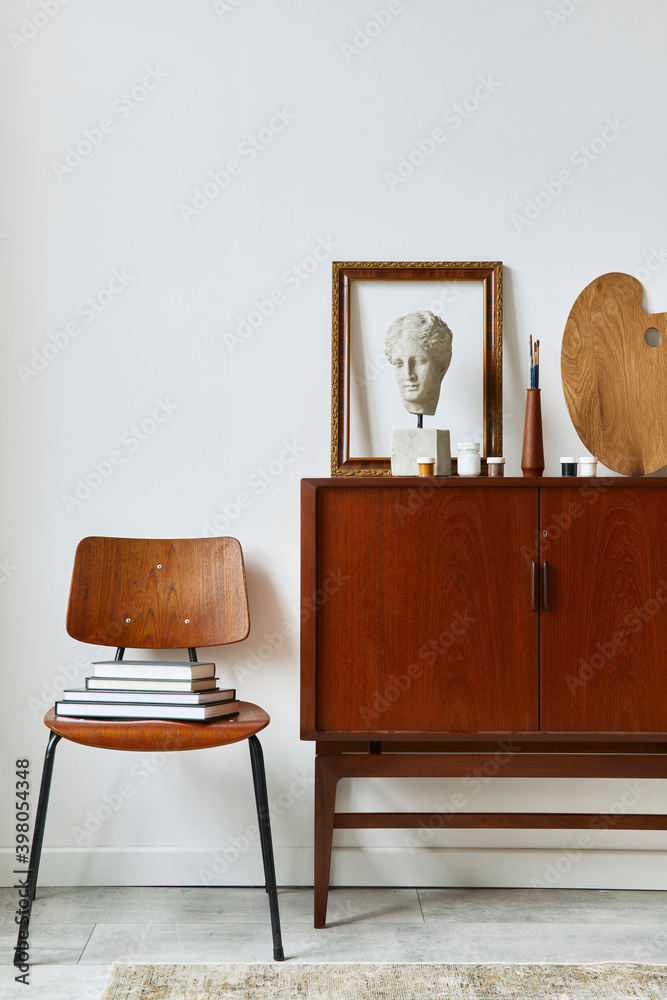 Stylish composition of artist workspace room with design teak commode, poster frames, easel, decoration and painting accessories. Template. Photo Adobe Stock