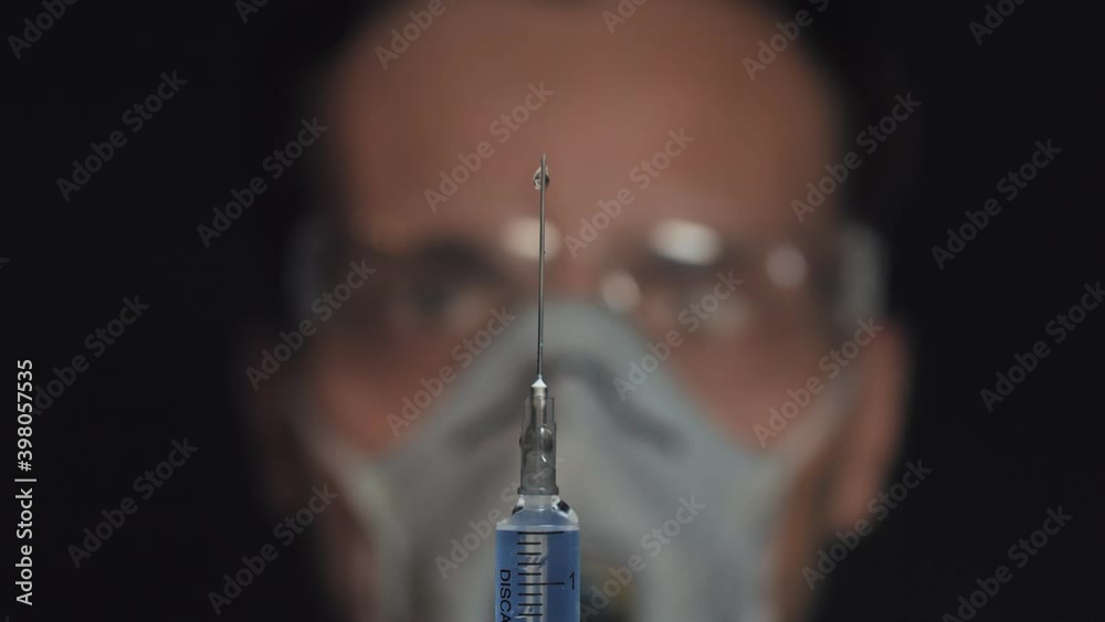 Doctor holds the syringe in his hand and presses the valve to release the air from the syringe,drops flow down the needle, preparing to injection.