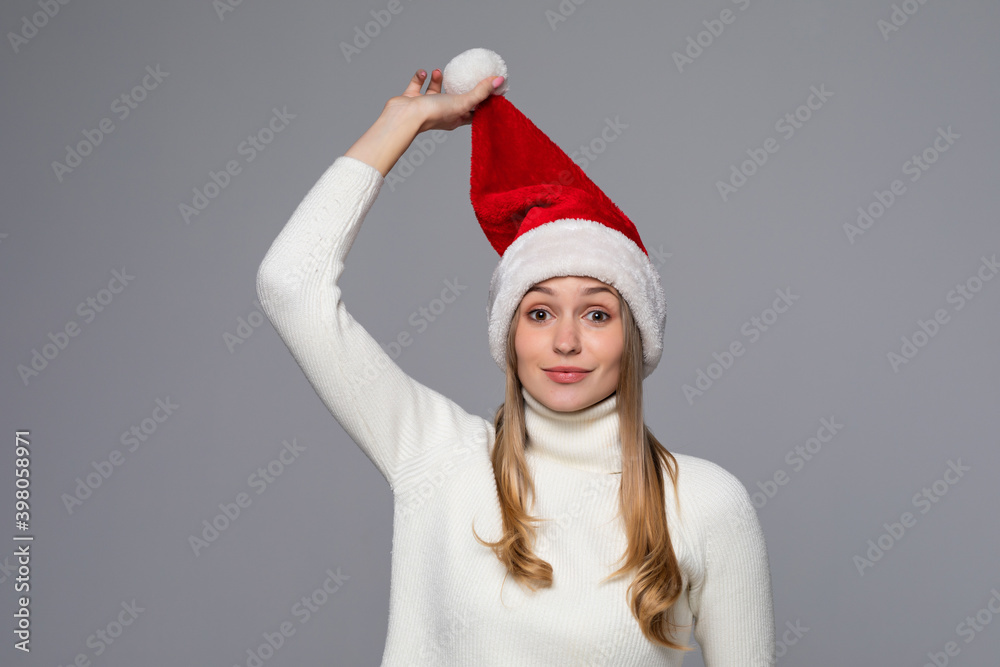 Smiling cute young woman in santa claus hat standing isolated over gray background Smiling cute young woman in santa claus hat standing isolated over gray background