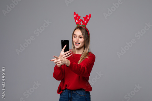 Happy charming woman with reindeer horns on her head holding phone on gray background. Christmas holidays. Copy space.