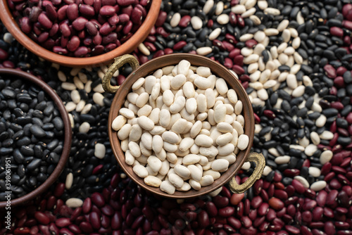 white beans in copper bowl, brown ceramic bowl and wooden bowl of beans. black bean, red kidney bean. navy bean, cannellini bean, white kidney bean. scattered various beans.