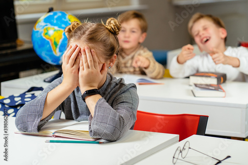 couple students bullying and suppress the guy sitting on the floor. Concept discrimination, racism and negative communication in school and society. Situations in school corridor photo