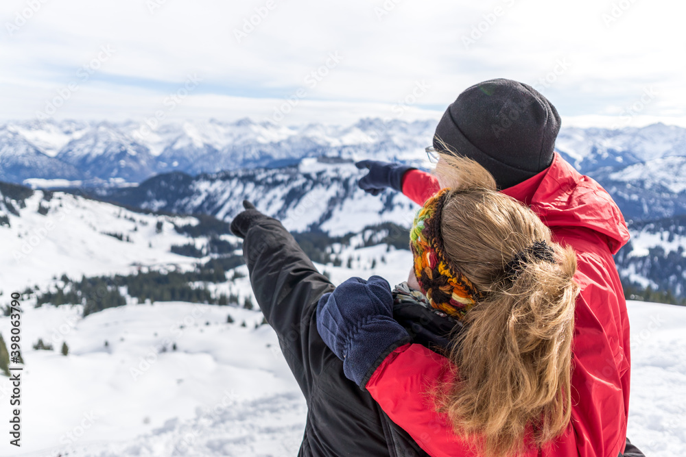 Senior couple is hiking in alpine snow winter mountains enjoying panorama view and pointing with finger to mountain peaks. Allgau, Bavaria, Germany.