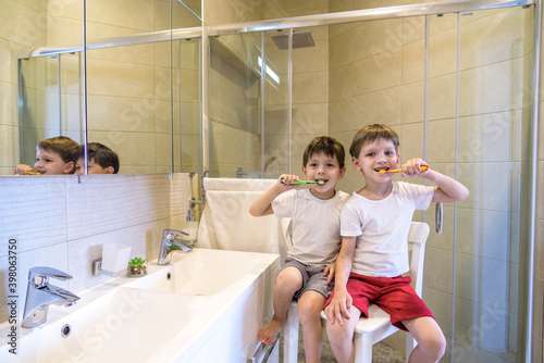 Closeup portrait of twins kids toddler boy brother in bathroom toilet washing face hands brushing teeth with toothbrush playing with water, lifestyle home style, everyday moments, morning routine.