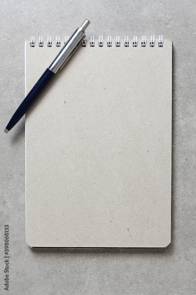 A spring notebook with a sheet of craft paper A5 with a ballpoint pen on light grey concrete background. Concept of new idea, business plan and strategy. Empty space for text A spring notebook with a sheet of craft paper A5 with a ballpoint pen on light grey concrete background. Concept of new idea, business plan and strategy. Empty space for text
