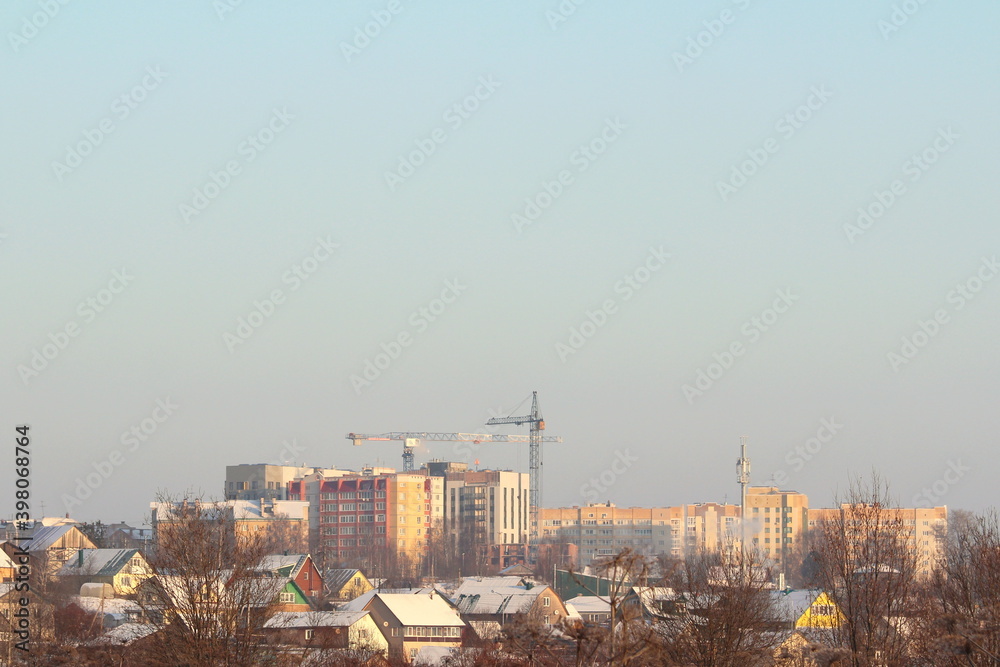 New modern multi-storey houses against the backdrop of small village houses on a clear winter day.