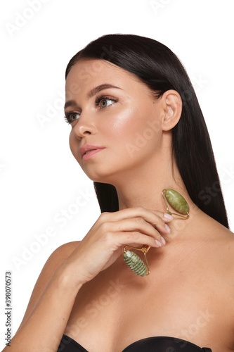 Beautiful young woman with perfect skin wearing towel on head using a jade face roller with natural quartz stones on white background