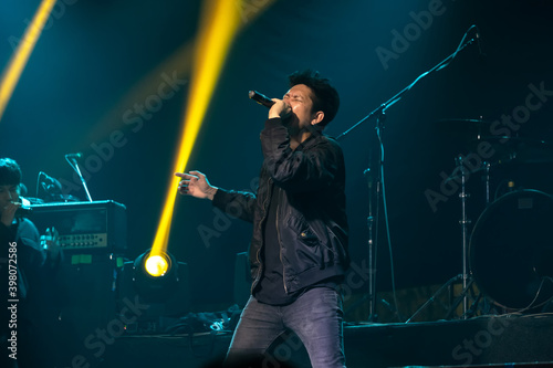 Photography A man singing rock music on the stage with a yellow spotlight and behind background is microphone and drum