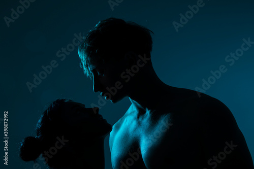 Beautiful man with his hot girlfriend is in the studio with blue neon lighting. Couple in love with each other. Couple love. Background. Neon. Light. 