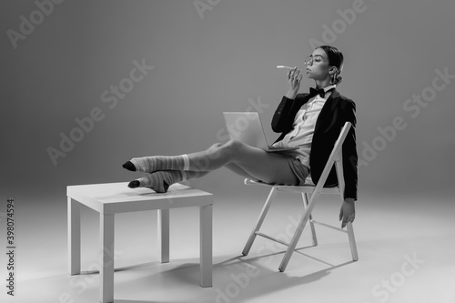 Gadgets. Young fashionable, stylish woman wearing jacket and socks working from home. Fashion during insulation 'cause of coronavirus pandemic. Half business and half home style. Black and white.