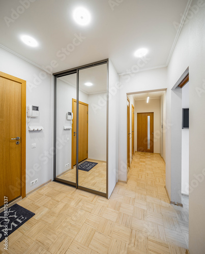 Modern interior of entrance hall in luxury apartment. Wooden door. Sliding door wardrobe with mirror. Narrow hallway.