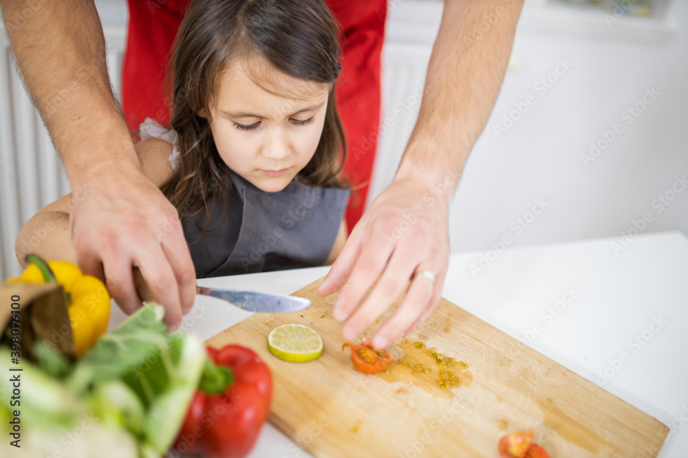 Little girl and her father slicing vegetables on a cutting board Little girl and her father slicing vegetables on a cutting board