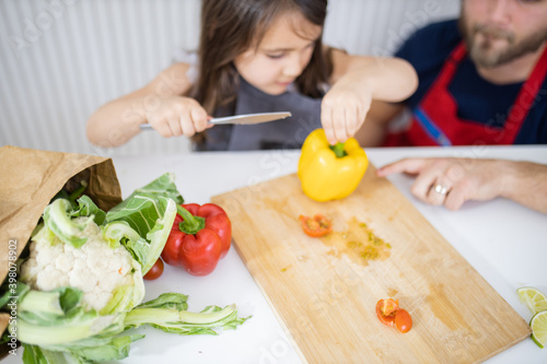 Little girl and her father slicing vegetables on a cutting board