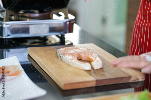 Hands of woman wearing red apron preparing healthy homemade recipe salmon fish in the kitchen for holiday festival. work from home new normal concept. 