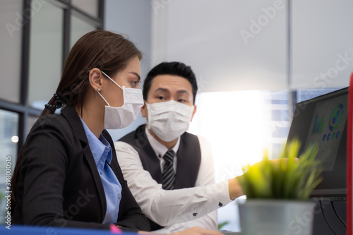 Two analysts with face masks discussing financial data on computer.