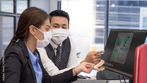 
Two analysts with face masks discussing financial data on computer.