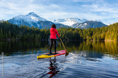 Adventurous Girl Paddle Boarding on Levette Lake with famous Tantalus Mountain Range in the background. Taken in Squamish, North of Vancouver, British Columbia, Canada.