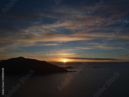 Beautiful aerial panorama view of peaceful sunset above Sessøya island, northern Norway in the Norwegian Sea with silhouettes of mountains and reflections in water.