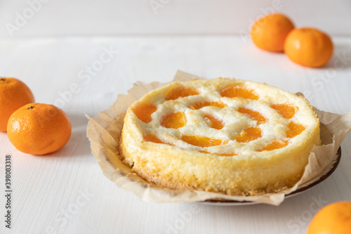 amerikanischer Cheesecake oder Käsekuchen mit orangen Mandarinen zur Weihnachtszeit im Winter auf einem Tisch aus Holz