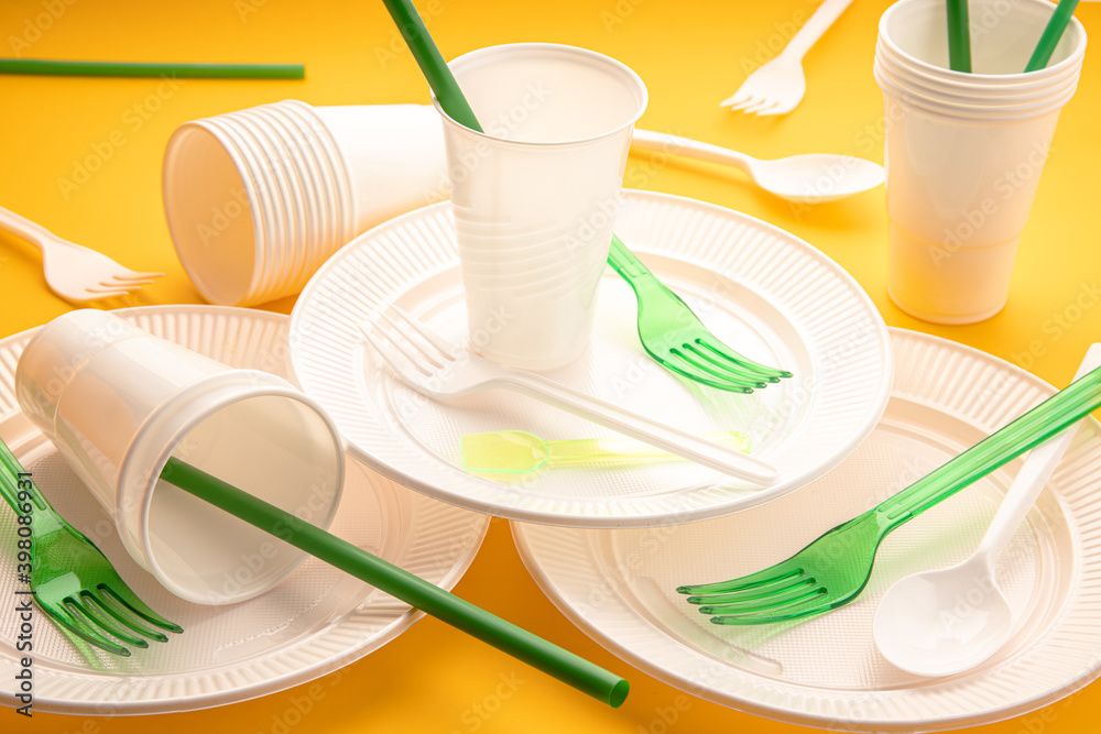 Disposable plastic dishware waste. Group of empty plates, cups, forks and  utensils on yellow table Stock Photo | Adobe Stock