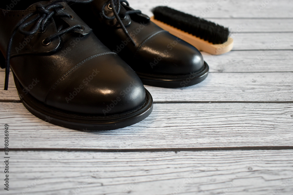 Black leather shoes and brush for cleaning shoes on a gray wooden background. A pair of stylish women's boots on the laminate floor, top view. Concept: Leather shoe care, shoe repair. space for text