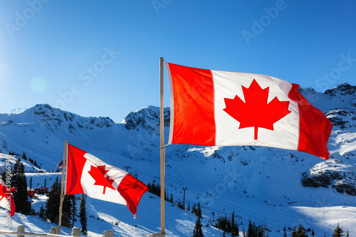 Canadian Flag with a winter mountain landscape in the background. Sunny morning blue sky. Taken in Whistler, British Columbia, Canada.