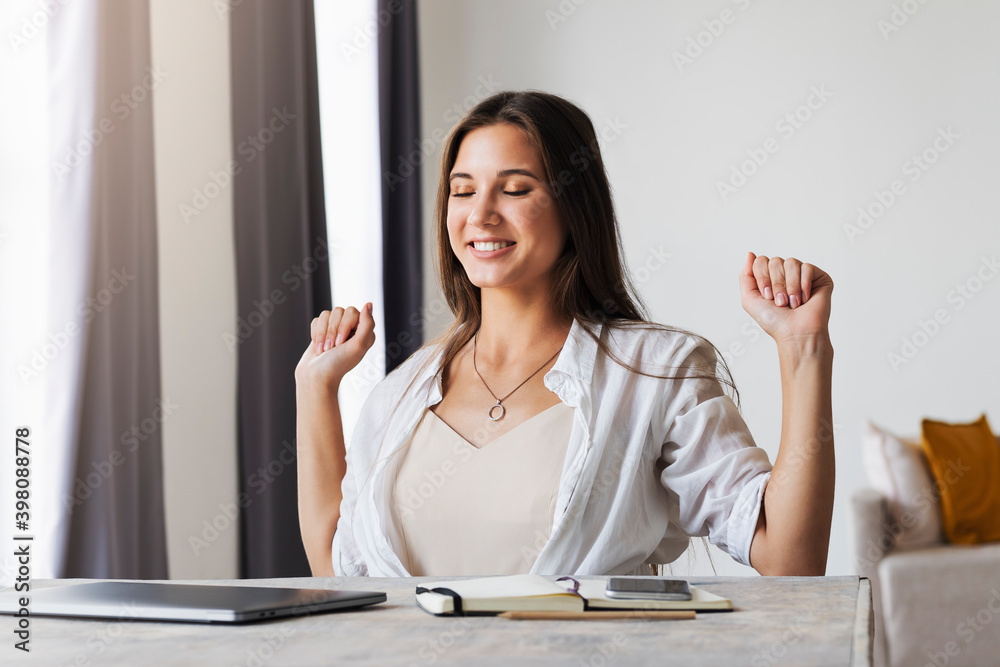 Beautiful brunette woman has completed business project, is happy. Girl sits at desk in home office. Distance work