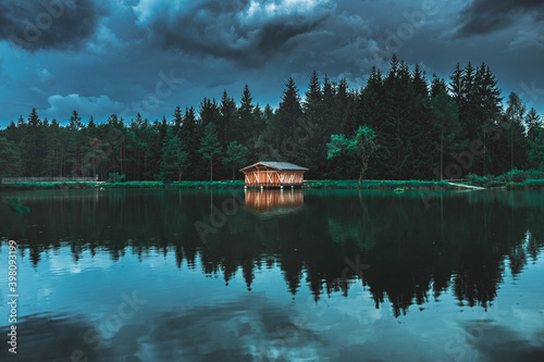 Wood house in a lake in a stormy day, blue mood, moody shot, bluish cast, dolomites, nature