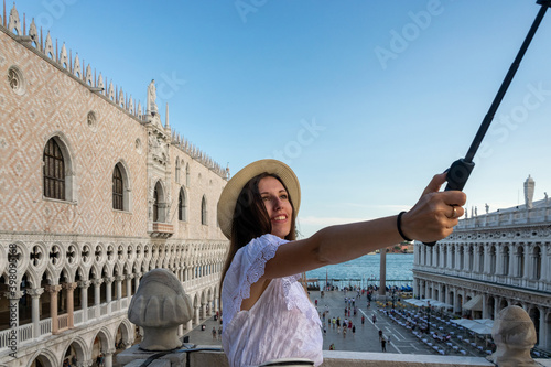 Pretty female taking fun self portrait photo in San Marco square in travel Europe city Italy, Venice. Panoramic view old Italian architecture with landmark bridge, romantic boat. Venezia. © Maksym