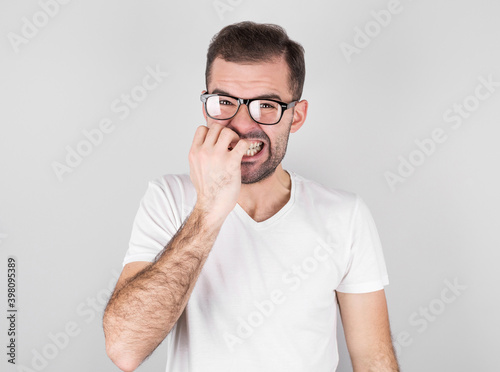 Portrait of joyful handsome bearded guy clenches teeth, blinks eye, bites nails over gray background