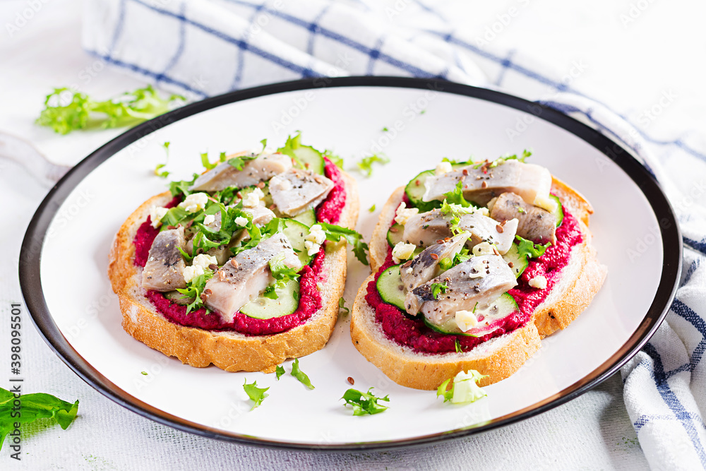 Herring fillet. Sandwich with salted herring and beetroot pate on the  toasts on white plate. Scandinavian cuisine.