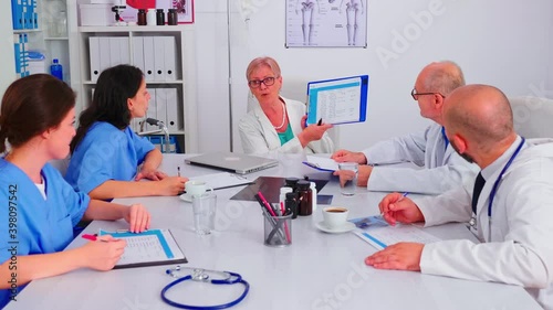 Medical women practitoner writing notes on clipboard wearing blue uniform during conference with coworkers. Clinic expert therapist talking with colleagues about disease, medicine professional. photo