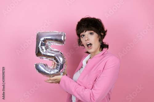Young business woman over isolated pink backgroundYoung business woman over isolated pink background smiling holding a number five balloon. Celebration concept photo