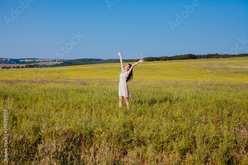 Beautiful woman in light dress walks on the field with flowers